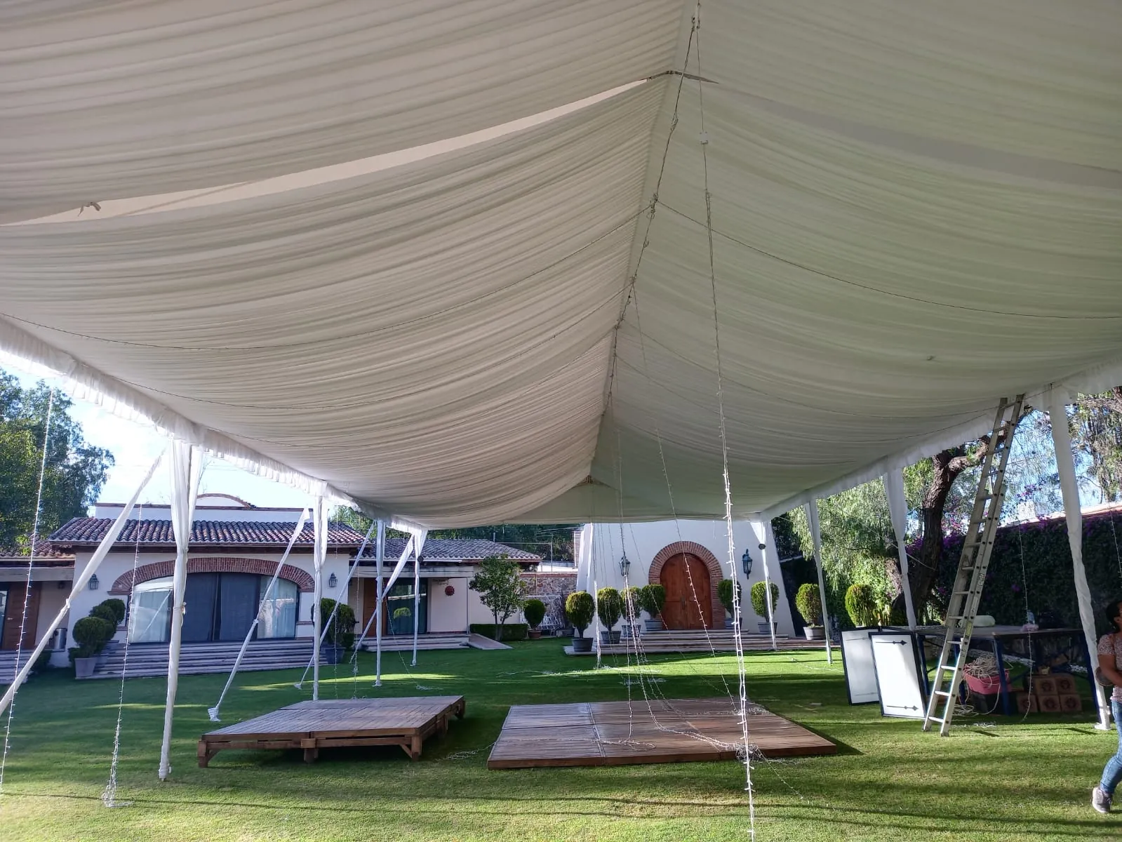 Interior de una carpa con techo drapeado en tela y tarimas de madera sobre el pasto